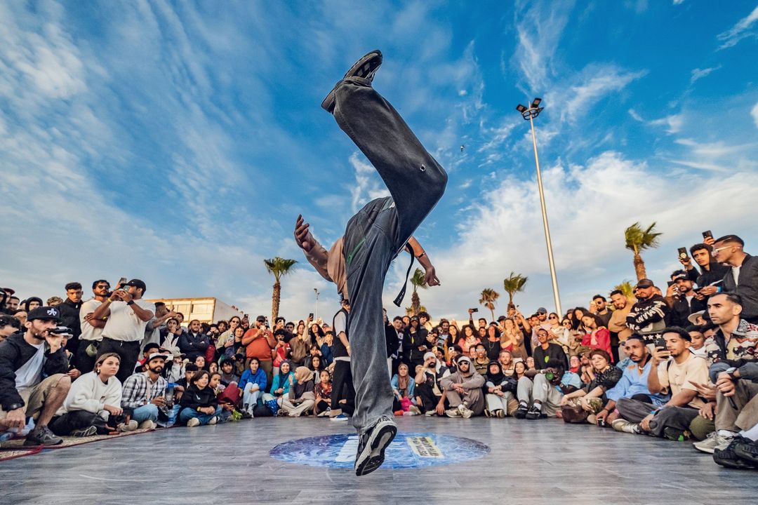 Un danseur sur la tête au centre du cercle, face à la foule de la corniche, en 2026